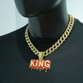 Close-up of golden Cuban chain with diamond KING pendant and red oil drip on black shirt - Pendant With Necklace / Gold