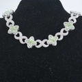 Macro shot of silver infinity links and green clover charms on a luxury Cuban necklace - Silver Green Stone