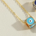 Golden cube necklace with blue evil eye enamel dice pendant on a textured surface - Blue