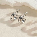Detailed view of silver C-shaped chunky hoop earrings with polished finish on stone surface - C-shaped Earrings / White Gold