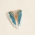 Detail showing crystal-encrusted angel wing brooch with teal feathers and golden finish - Blue Wings