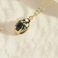 Macro shot of an oval black enamel pendant with golden floral motifs on a fine chain - Black (MA1-8)