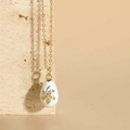 Macro shot of gold-plated egg pendant with white enamel flower and zircon inlay details - White