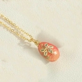 Macro shot of red enamel egg pendant with gold floral pattern and sparkling crystals - Orange