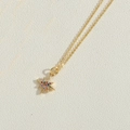 Detailed close-up of a gold starburst pendant with colorful zircon stones on a fine chain - Octagram Star Style / Gold