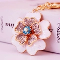 Eleganter Blumen-Schlüsselanhänger mit weißen Blütenblättern und Kristallen auf Gold - Blau