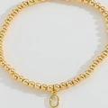 Minimalist gold beaded bracelet featuring a polished metallic letter O pendant charm - Letter O