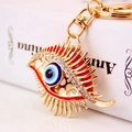 Llavero de ojo turco dorado con diamantes de imitación y pestañas sobre un libro - Rojo