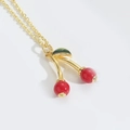 Collana chic con ciondolo a ciliegia rossa, foglia dorata e frutto in resina su sfondo bianco - Piccola Ciliegia