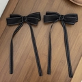 Close-up of black ribbon bow hair clips with white stitching on dark wooden background - Bow Ribbon Style / Black