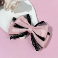 Close-up of pink satin bow hair clip with delicate black lace trim on a white plate - Pink