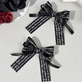 Detailansicht von zwei schwarzen Satin-Schleifenclips mit künstlerischem weißem Textdruck - Schwarz Buchstaben Stil