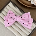 Detailed close-up of a pink striped bow hair clip with black heart patterns on display - Pink