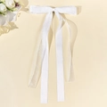 Détail d'une pince à cheveux avec nœud en tulle blanc et longs rubans sur fond beige - Blanc