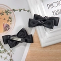 Detail showing two black satin double-layered bow hair clips with silver metal duckbill base - Black
