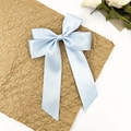 Détail de la pince à cheveux nœud en satin bleu clair avec de longs rubans sur fond texturé - Bleu