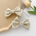 Lot de barrettes à nœuds en satin crème avec strass en cœur sur un plateau beige - Paire / Champagne