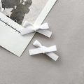 Detalle de dos pinzas para el cabello con lazo blanco y diseño cruzado en fondo gris - Blanco