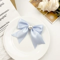 Macro detail of elegant light blue satin bow hair clip with large centered faux pearl inlay - Blue