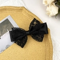 Close-up of elegant black lace bow hair clip on a textured tray with white roses - Black