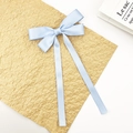 Close-up of light blue satin bow hair clip with long ribbons on textured paper - Blue