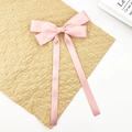 Close-up of pink satin ribbon hair clip with long streamers on textured background - Pink
