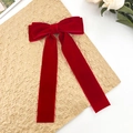 Macro detail of red velvet bow hair clip with long streamers on a textured gold background - Red