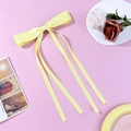 Pale yellow satin bow hair clip with long ribbons on a pink decorative background - Yellow