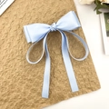 Detailed view of light blue satin bow hair clip with long ribbons on brown background - Blue