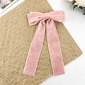 Detailed close-up of pink velvet bow hair clip with long streamers on textured paper - Pink