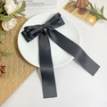 Détail d'un élégant nœud à cheveux en satin noir avec rubans posé sur une assiette blanche - Noir