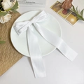 Détail d'une barrette à cheveux nœud en satin blanc élégant sur une assiette décorative - Blanc