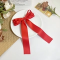 Détail d'un nœud papillon en satin rouge avec de longs rubans sur une assiette décorative - Rouge