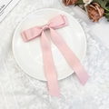 Detail view of pink satin bow hair clip with long streamers on white lace background - Pink