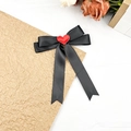 Detailansicht einer schwarzen Satin-Haarschleife mit rotem Herz auf braunem Papierhintergrund - Mittlerer Schwalbenschwanz-Bandstil / Schwarz