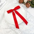 Detail view of a red satin bow hair clip with long ribbons on a decorative plate - Red