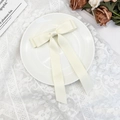 Detailed view of elegant cream satin bow hair clip with long ribbons on a lace tablecloth - Beige