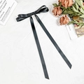 Close-up of a black satin bow hair clip with long ribbons on white textured fabric - Black