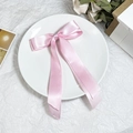 Detail einer rosa Satin-Schleifen-Haarklammer mit Bändern auf elegantem weißem Hintergrund - Rosa