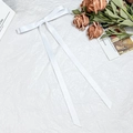 Detailed view of elegant white satin bow hair clip with long ribbons on textured paper - White
