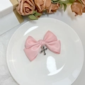 Dettaglio molletta a fiocco in raso rosa con ciondolo a croce d'argento su ceramica bianca - Rosa Croce