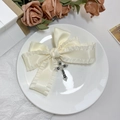 Nahaufnahme der cremefarbenen Satin-Schleife mit schwarzem Kreuzanhänger auf Dekoteller - Beige