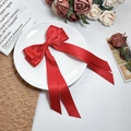 Close-up of elegant red satin bow hair clip with long ribbons on a white porcelain plate - Red