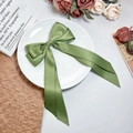Detailed view of an olive green satin ribbon hair bow on a white vintage ceramic plate - Green