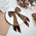Detail of coffee brown satin bow hair clip with elegant ribbons on white ceramic plate - Brown