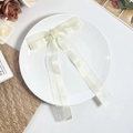 Close-up of cream white satin bow hair clip with elegant long ribbons on a ceramic plate - Beige