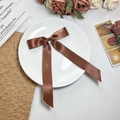 Detailopname van een donkerbruine satijnen strik haarclip op een vintage decoratief bord - Bruin