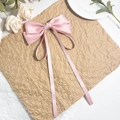 Detailansicht der rosa Satin-Schleife Haarklammer mit langen Bändern auf Kraftpapier - Rosa