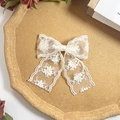 Detailed close-up of embroidered lace bow hair clip with floral patterns on cork tray - White