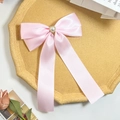 Dettaglio del fiocco in raso rosa con perla a cuore su un vassoio vintage - Rosa